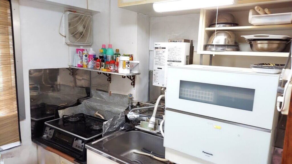 足立区の高齢者宅キッチンの作業前の様子。油汚れが付いたガス台とプロペラ式換気扇、シンク周りを家事代行・掃除代行サービス前に撮影