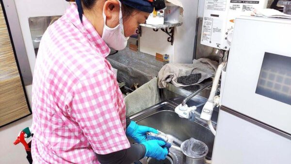 足立区の高齢者宅キッチンでシンク排水口を洗浄している作業風景。家事代行・掃除代行サービスによる清掃中の写真